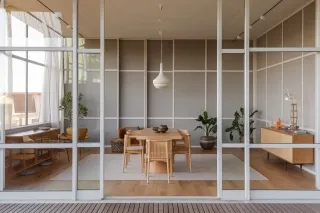 Un intérieur moderne avec une salle à manger minimaliste comprenant une table en bois, des chaises assorties et des plantes décoratives, visible à travers