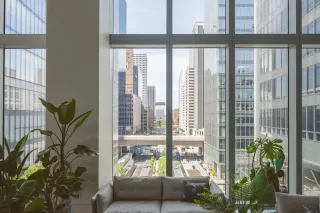 Un canapé confortable entouré de plantes vertes offre une vue panoramique sur une ville moderne à travers de grandes fenêtres.