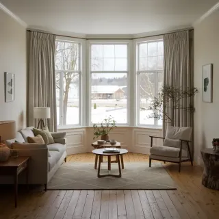 Un salon lumineux et cosy avec de grandes fenêtres, un canapé confortable, une table basse en bois et une vue sur l'extérieur enneigé.