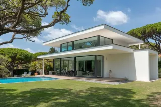 Maison contemporaine avec grandes baies vitrées, piscine et jardin verdoyant sous un ciel bleu.