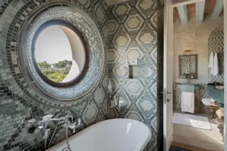 Salle de bain élégante avec mosaïque géométrique bleue et fenêtre circulaire offrant une vue pittoresque.