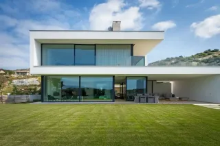 Voici une maison moderne à deux étages aux lignes épurées, avec de grandes baies vitrées et vue sur un jardin bien entretenu.