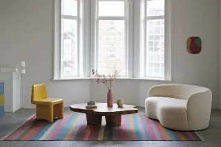 Un salon moderne lumineux avec des meubles contemporains, comprenant une table basse en bois, une chaise jaune, un canapé blanc et un tapis rayé color