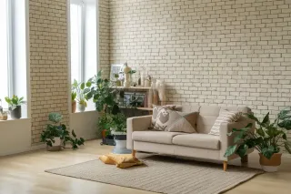 Salon moderne avec un canapé beige, plantes vertes et mur en briques blanches.