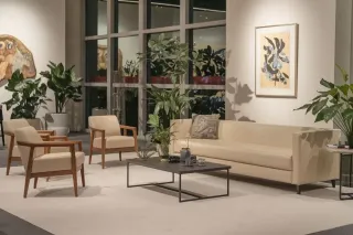 Un salon élégant et moderne avec un canapé beige, deux fauteuils assortis, une table basse noire et plusieurs plantes vertes, baigné de lumière