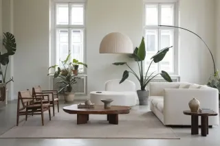 Un salon moderne et épuré, décoré de plantes vertes, avec des meubles en bois et un canapé blanc, baigné de lumière naturelle.