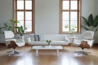 Un salon lumineux et minimaliste avec un canapé blanc, deux fauteuils modernes, une table basse, et des plantes vertes devant de grandes fenêtres en