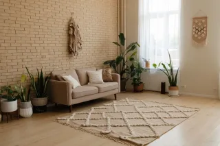 Un salon lumineux au style minimaliste avec un canapé beige, un tapis à motifs géométriques et des plantes d'intérieur, offrant une ambiance chaleureuse