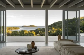 Cette image montre un intérieur moderne et lumineux avec une vue imprenable sur la mer et des îles verdoyantes à travers de grandes baies vitr