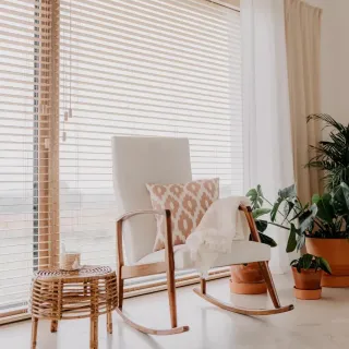 Un fauteuil à bascule blanc avec un coussin à motifs géométriques se trouve près d'une fenêtre ensoleillée, entouré de plantes en