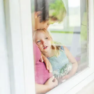 Deux enfants regardent pensivement par une fenêtre, l'aîné serrant tendrement le plus jeune contre lui.