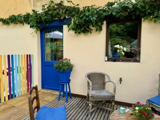 La terrasse colorée et fleurie comporte des chaises en osier et une porte bleue, offrant un espace convivial et accueillant.