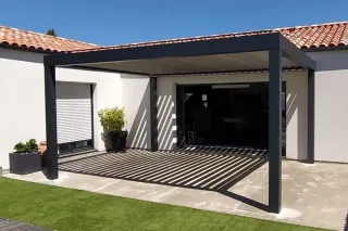 Une maison moderne avec pergola en métal noir surplombant une terrasse partiellement ombragée, entourée de murs blancs et de tuil