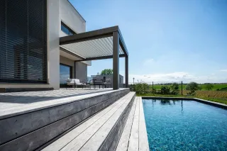 Terrasse en bois moderne avec pergola ouverte, donnant sur une piscine et une vue dégagée sur la campagne.