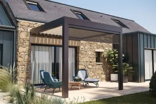 Une terrasse moderne avec pergola bioclimatique, adossée à une maison en pierre, aménagée de chaises en osier et entour