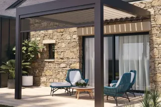 Une terrasse élégante avec des fauteuils en osier bleu sous une pergola moderne adossée à un mur en pierre.