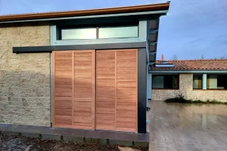 Façade moderne avec volets en bois clair et murs en pierre naturelle, intégrée dans un environnement résidentiel.