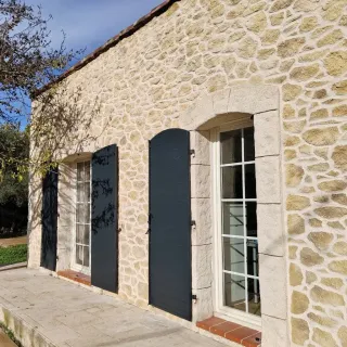 Façade en pierre d'une maison traditionnelle avec des volets en bois sombre.