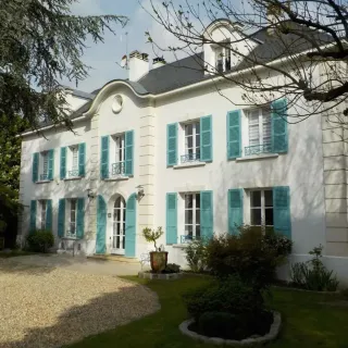 Belle maison traditionnelle avec volets turquoise et façades blanches, entourée d'un jardin verdoyant.