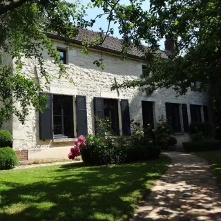 Charmante maison en pierres avec volets noirs et jardin fleuri sous un ciel bleu.