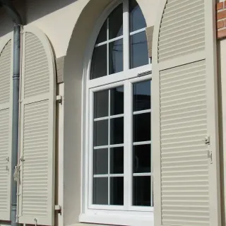 Fenêtre en PVC blanc à double vitrage avec volets en bois clair, offrant une touche élégante et fonctionnelle à la façade.