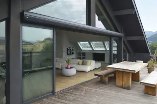 Une terrasse en bois moderne avec de grandes portes vitrées donnant sur un salon lumineux et spacieux.