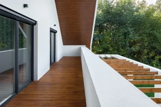 Une terrasse moderne en bois avec des garde-corps blancs et vue sur la verdure environnante.