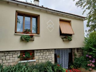 Façade d'une maison avec des fenêtres en bois ornées de jardinières fleuries et une porte d'entrée en bas entourée de végét