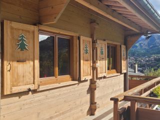 Vue extérieure d'un chalet en bois avec des volets décorés d'arbres, surplombant un paysage montagneux.