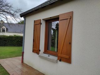 Une fenêtre en bois avec des volets fermés sur un mur clair, entourée d'une pelouse verte.