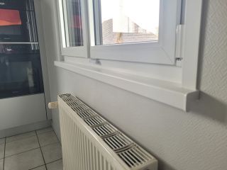 L'image montre un intérieur de cuisine moderne avec une fenêtre à double vitrage et un radiateur blanc, offrant une vue partielle vers l'extérieur.