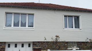 Façade d'une maison avec un revêtement en vinyle blanc, un toit en tuiles rouges et deux grandes fenêtres.