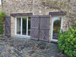 Façade en pierre avec fenêtres à volets en bois, donnant sur une cour en pavés entourée de verdure.