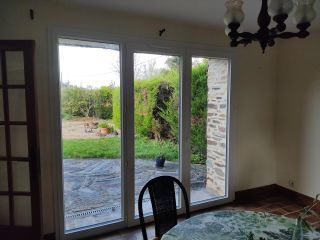 Une baie vitrée s'ouvre sur un jardin verdoyant, offrant une vue apaisante depuis l'intérieur d'une maison.