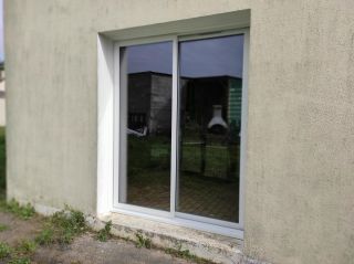 Une fenêtre en verre, intégrée dans un mur beige, reflète un jardin extérieur.