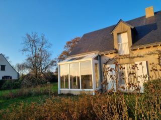 Maison avec véranda lumineuse sur jardin verdoyant en fin de journée.