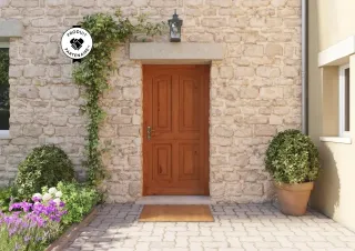 Porte d'entrée en bois massif ornée de plantes grimpantes et entourée d'un jardin fleuri, sur une façade en pierre.