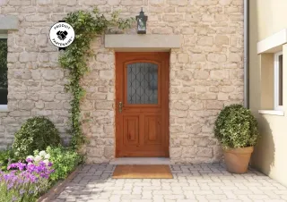 Entrée de maison en pierre avec une porte en bois, décorée de plantes grimpantes et d'arbustes en pot.