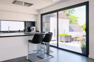 Cuisine moderne et lumineuse avec des fenêtres coulissantes donnant sur une terrasse extérieure.