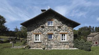 Volets pliants blancs sur facade maison en pierre en montagne