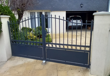 Portail en fer forgé noir ouvrant sur une allée menant à une maison moderne avec une voiture garée à l'intérieur du garage.