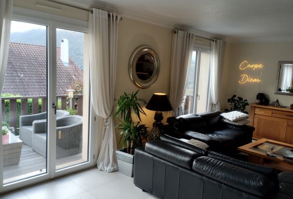 Un salon élégant avec des canapés en cuir noir, une décoration moderne, et une terrasse extérieure visible par des portes-fenêtres.