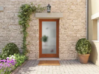 Entrée de maison charmante avec porte en bois vitrée et mur en pierres, entourée de plantes vertes et de fleurs colorées.