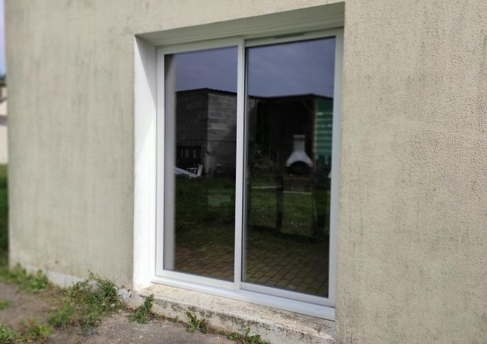 Une fenêtre en verre, intégrée dans un mur beige, reflète un jardin extérieur.