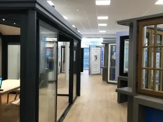 Un showroom moderne avec des présentations de portes et fenêtres sur un sol en bois clair.