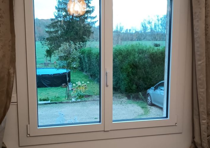 Fenêtre en PVC blanc avec vue sur un jardin verdoyant, un arbre et une piscine extérieure couverte.