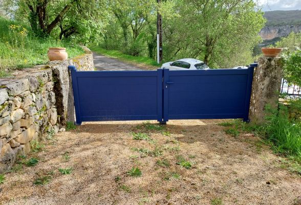 Une porte en bois bleue, entourée de murs en pierres avec des pots de fleurs, donne sur une allée verdoyante sous un ciel