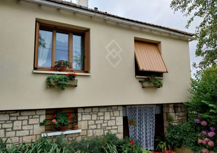 Façade d'une maison avec des fenêtres en bois ornées de jardinières fleuries et une porte d'entrée en bas entourée de végét