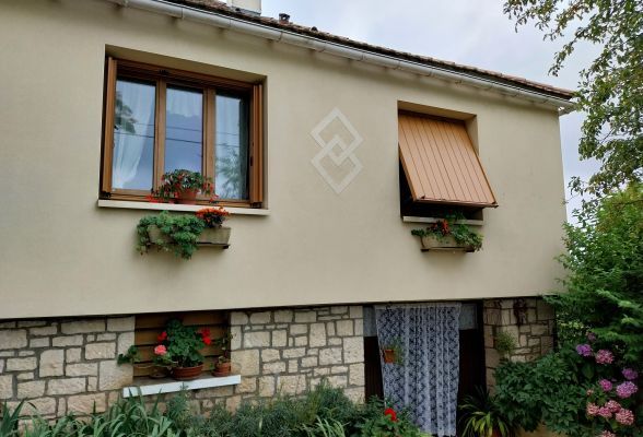 Façade d'une maison avec des fenêtres en bois ornées de jardinières fleuries et une porte d'entrée en bas entourée de végét