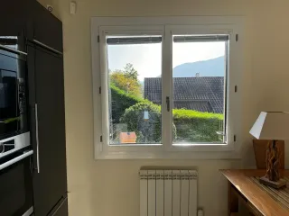 Une cuisine lumineuse avec une fenêtre offrant une vue sur un jardin et des montagnes au loin.